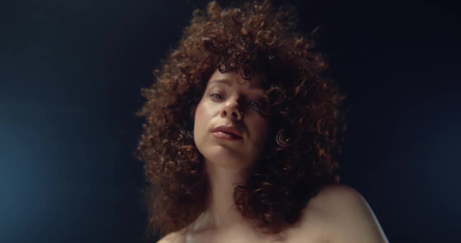 A shirtless curly haired female posing