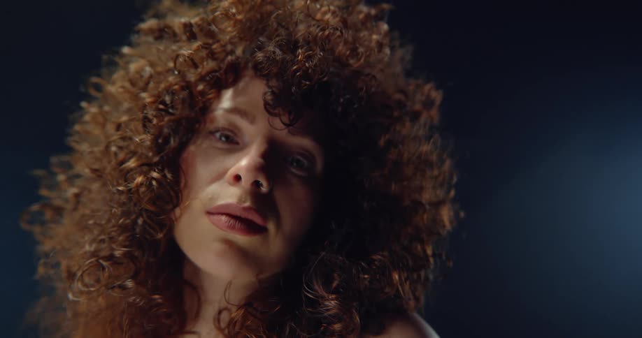 Woman with curly hair and piercing looks down at camera in the stuido