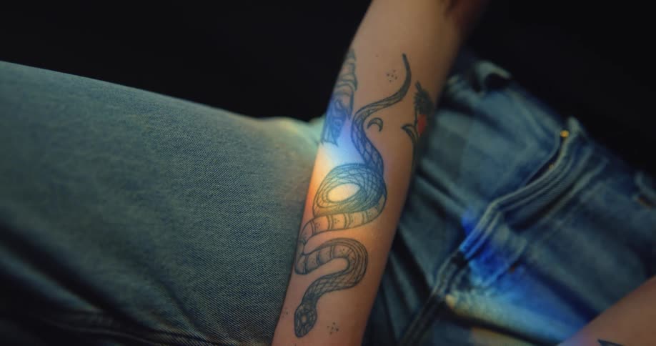 A man is sitting in a chair with tattoos on his arms and light is shining on a snake on his right forearm