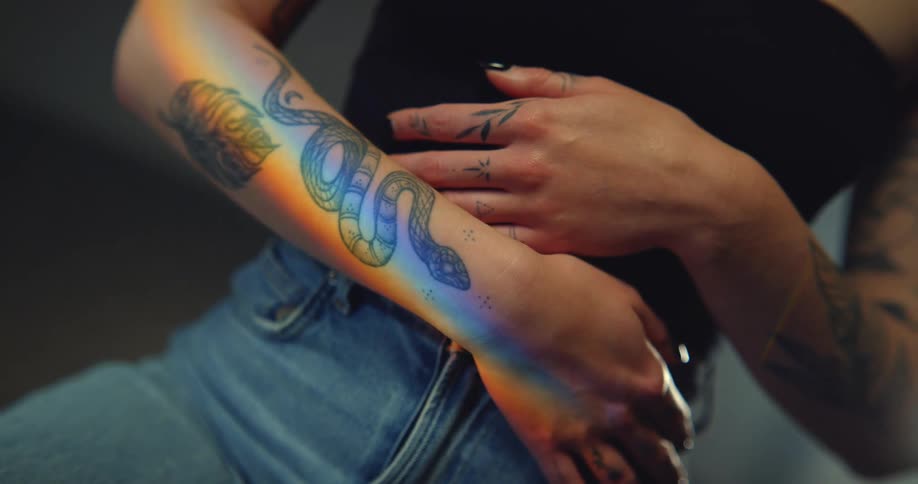 Close up of female models arm with tattoos black top and jeans in the studio