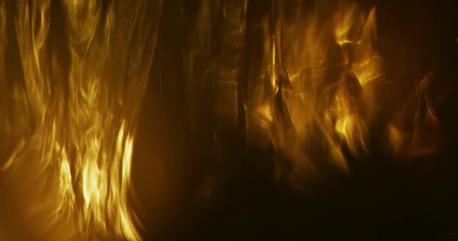 A fluid swirls in the darkness as it is illuminated by orange light