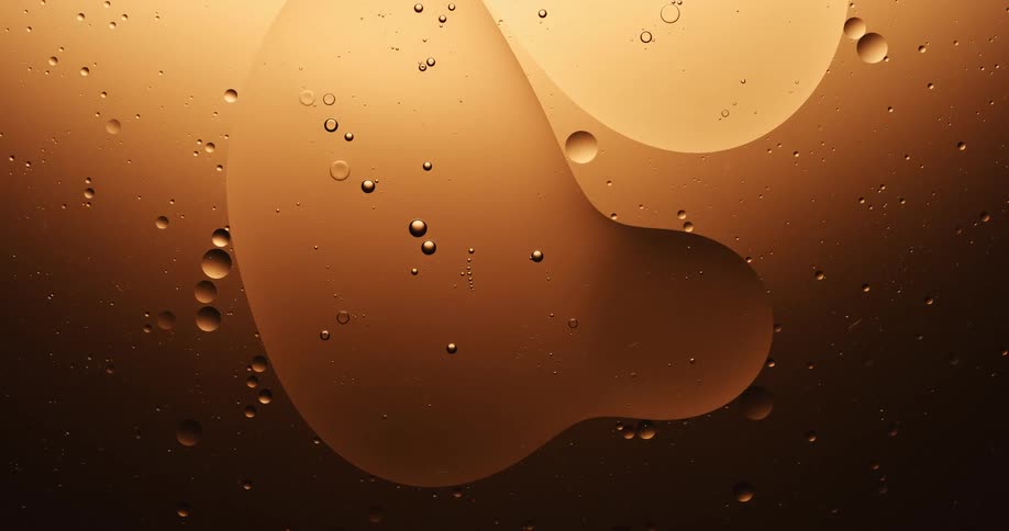 Many spheres of various sizes are floating in a golden substance with bubbles inside of them and around the outside edges as one of them splits into three orbs