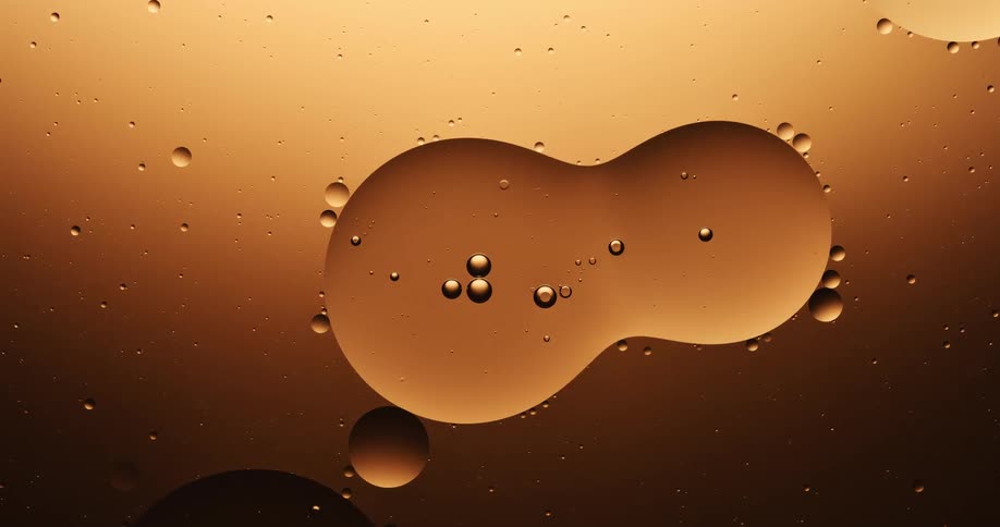 Many spheres of various sizes are floating in a golden substance with bubbles inside of them and around the outside edges as one of them splits into two orbs