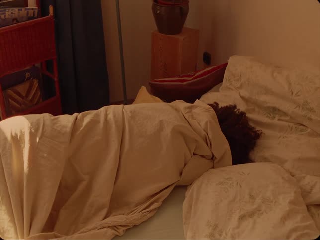 A man rolls his girlfriend up in a blanket while she lies in bed