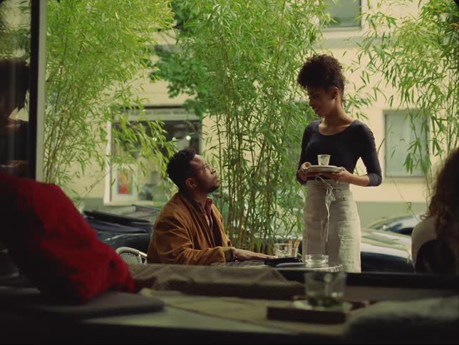 A male customer converses with a female waitress while he sits outside