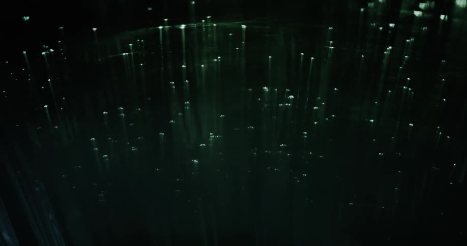 Blue and green lights glow on the ends of thin illuminated fiber moving in the darkness