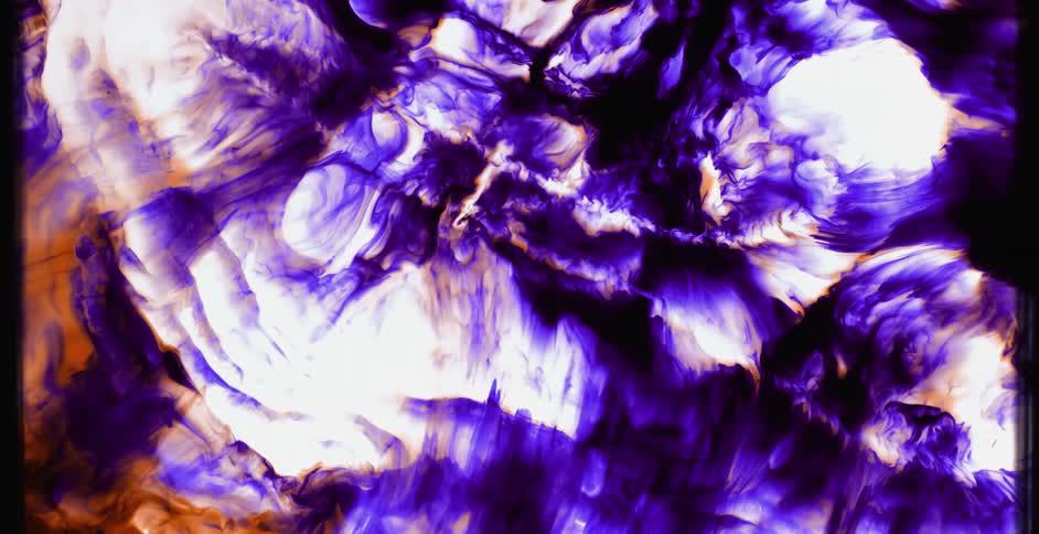 A purple and orange substance is moving across glowing white area in the darkness