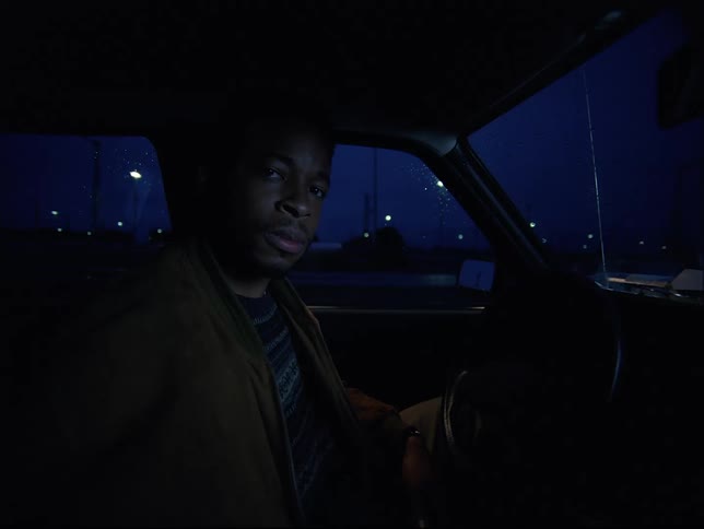 A man is sitting in the drivers seat of an automobile at night looking toward the passenger seat