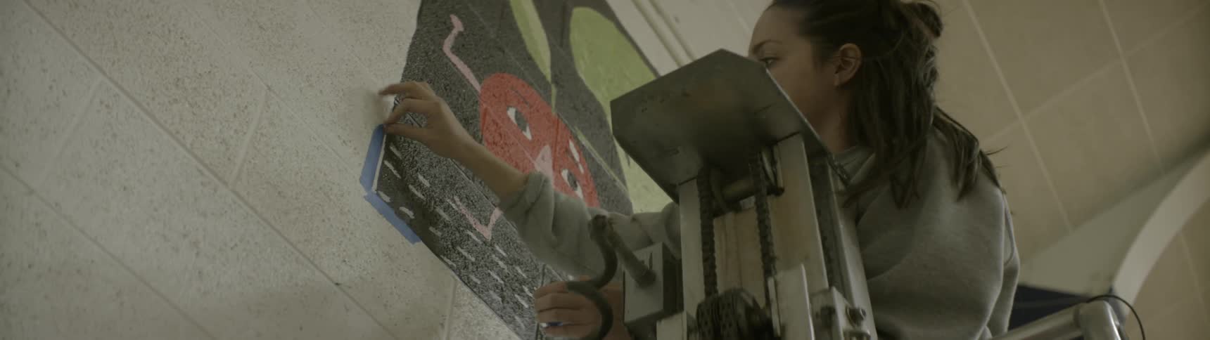 A woman pulls blue tape away from a painting on the wall
