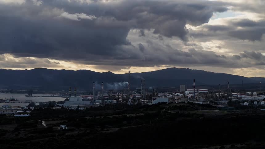 Time lapse of dark clouds moving over polluting factory smokestacks on the shore