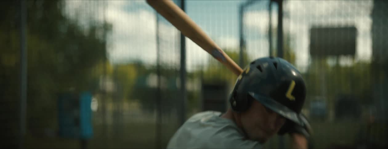 Baseball player wearing a helmet swings his bat on the field at daytime