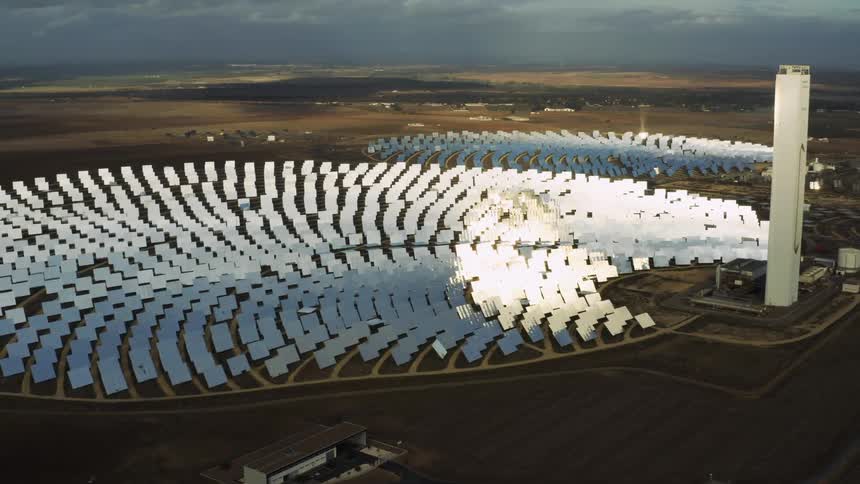 Sunlight moves over a circular field of solar panels in the countryside on a cloudy day