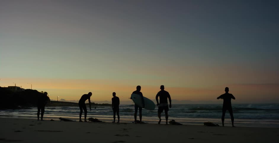 Men with surf boards stretch on the shore