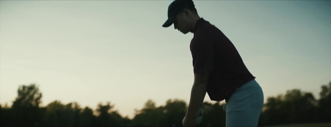 Golfer swings and hits a ball on a field at evening