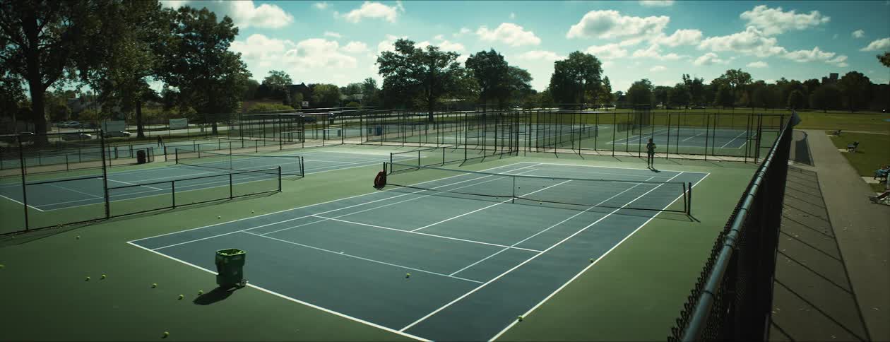 A person practices hitting tennis balls on an outdoor tennis court during the day