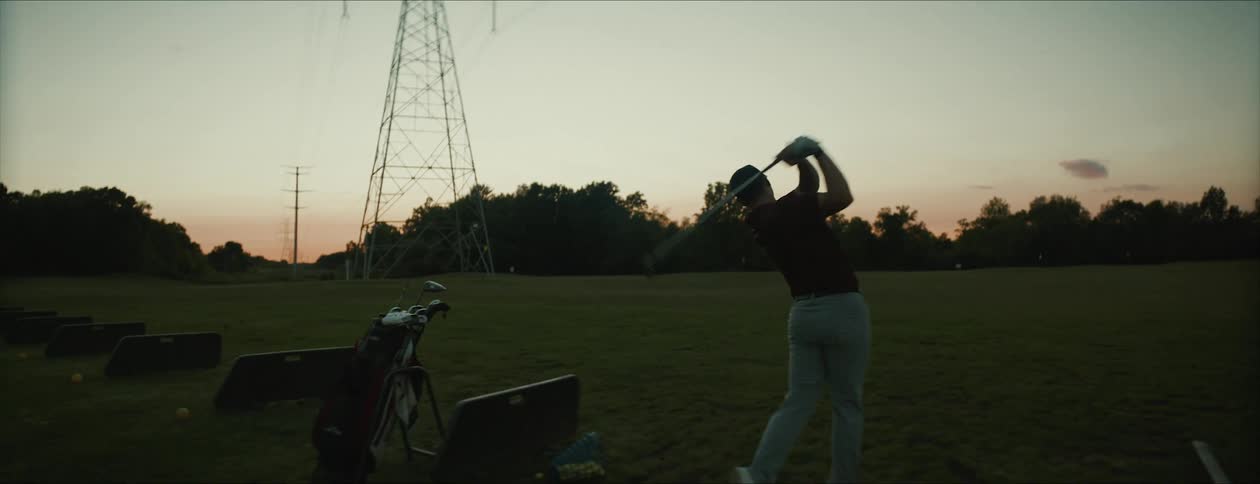 A man swings his golf club on a practice course in the morning