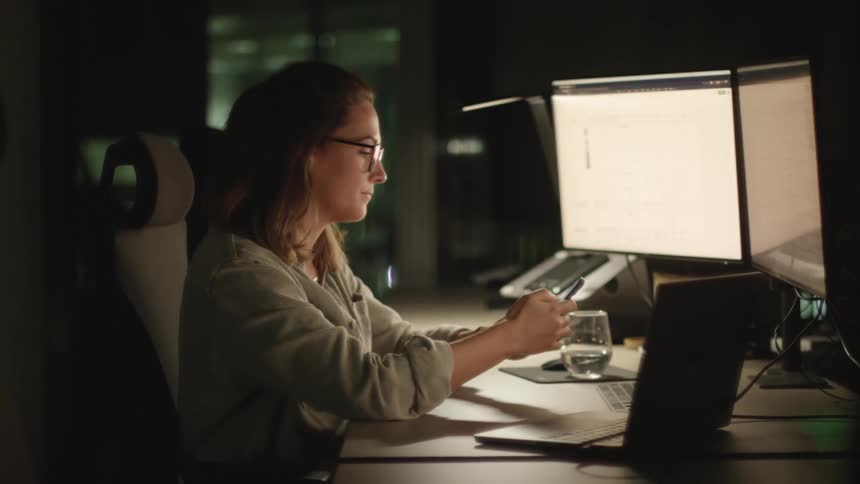 A young white woman is working in the office and on her phone