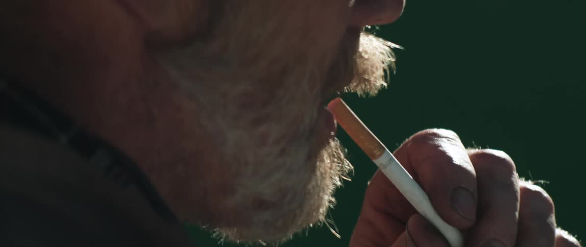 A man who is outside puts a cigarette in his mouth