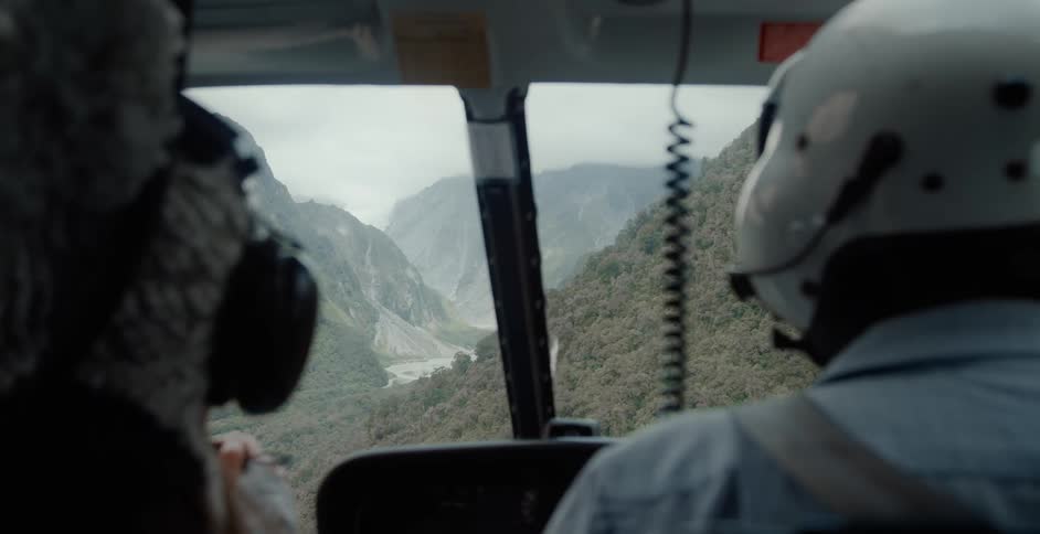 Two people are flying in a helicopter in the wilderness