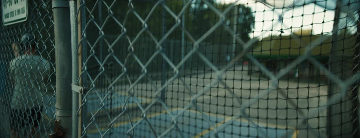 A batter enters an outdoor batting cage and takes a batting stance