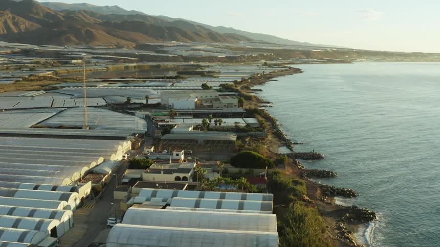 Metal grain silos sit side by side along the sea coast below a mountain range