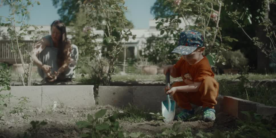 A boy helps his mom shovel dirt in a garden plot