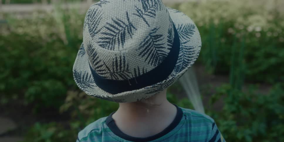 A young boy waters plants outside