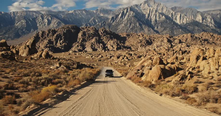 Black vehicle drives on a dirt road away from the mountain range