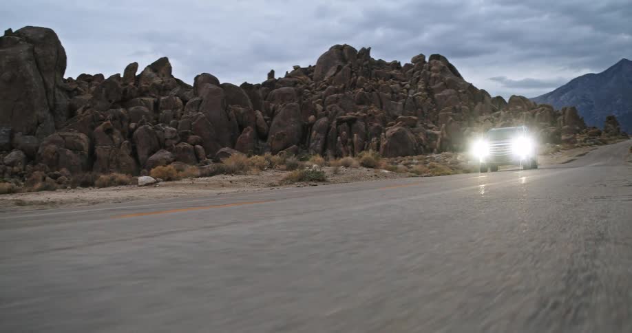 A vehicle travels along a road through the badlands on a cloudy evening