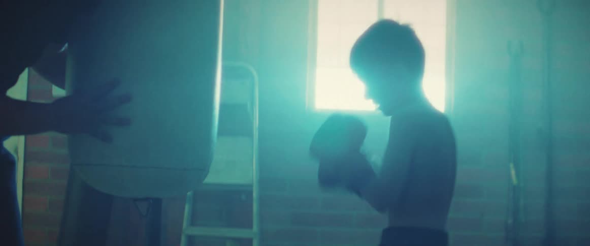 Determined shirtless boxer boy hits punching bag in the gym