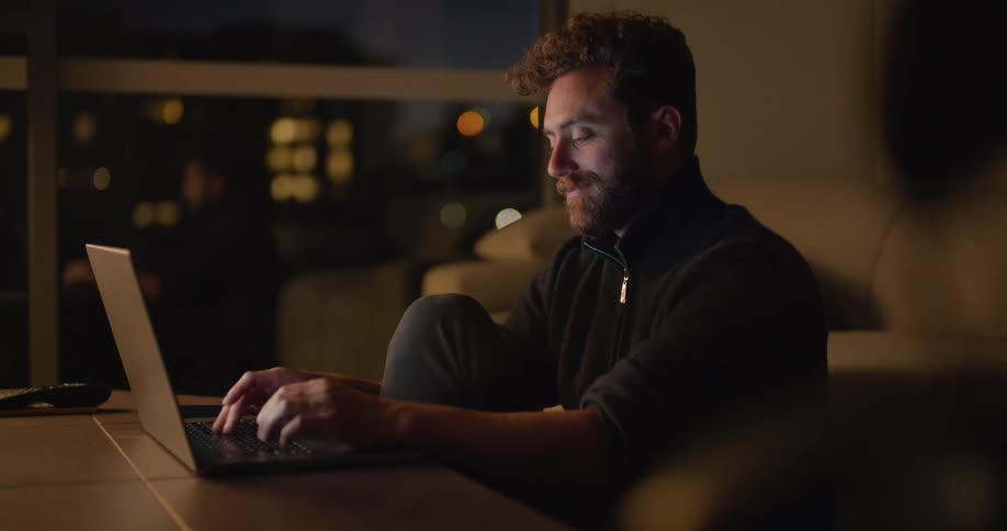 A man uses a laptop while sitting on the floor at table at night