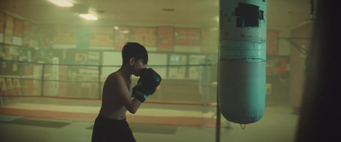 A young kid is boxing inside of a gym in the day time