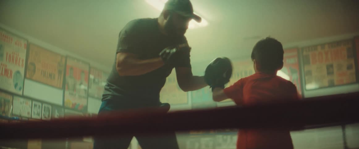 Adult male trains boy wearing boxing gloves in boxing ring