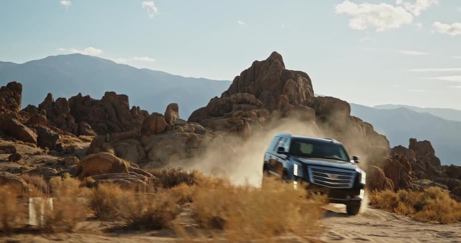 A truck travels on a dirt road among rock formations and mountains in the desert badlands