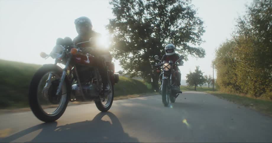 Two women speeding down a country road on motorcycles