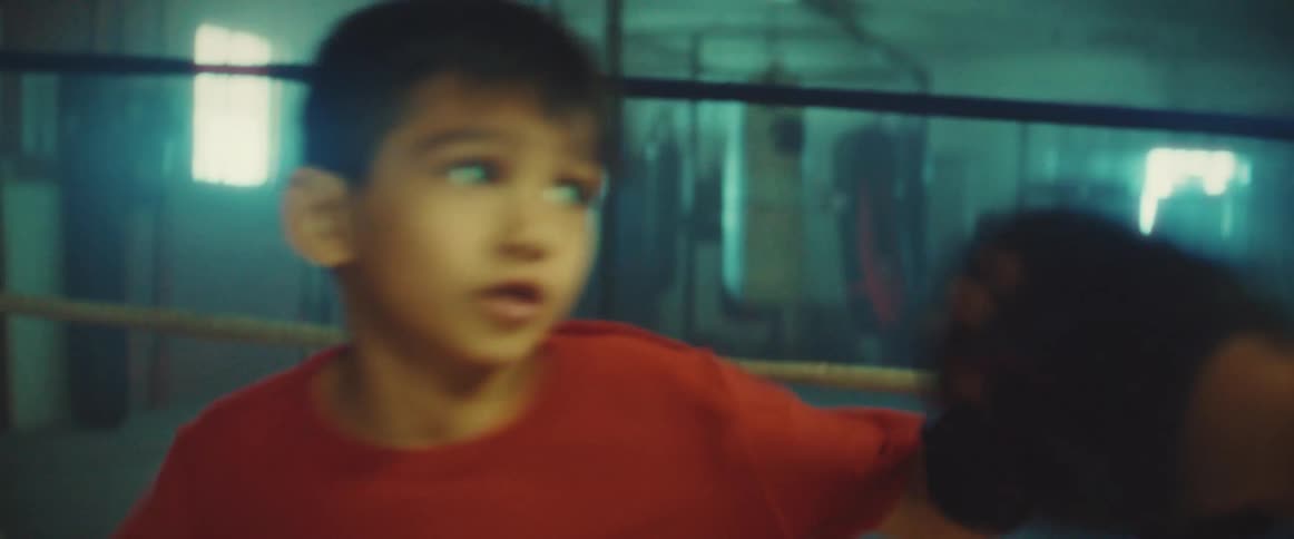 A boy practices boxing with a trainer in a boxing ring during the day