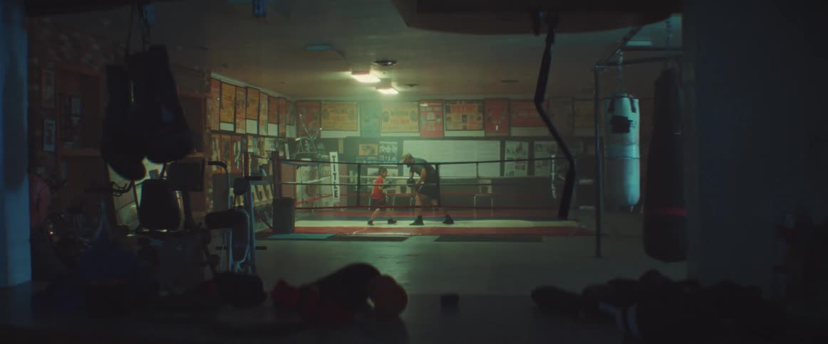 Man trains boy in boxing ring set in dimly lit boxing gym