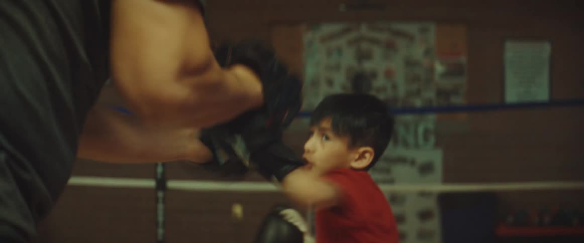 A little boy throws punches as he boxes in a ring with a man