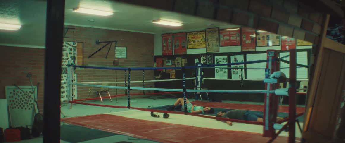 Two people are laying faceup on the floor of a boxing ring in a gym