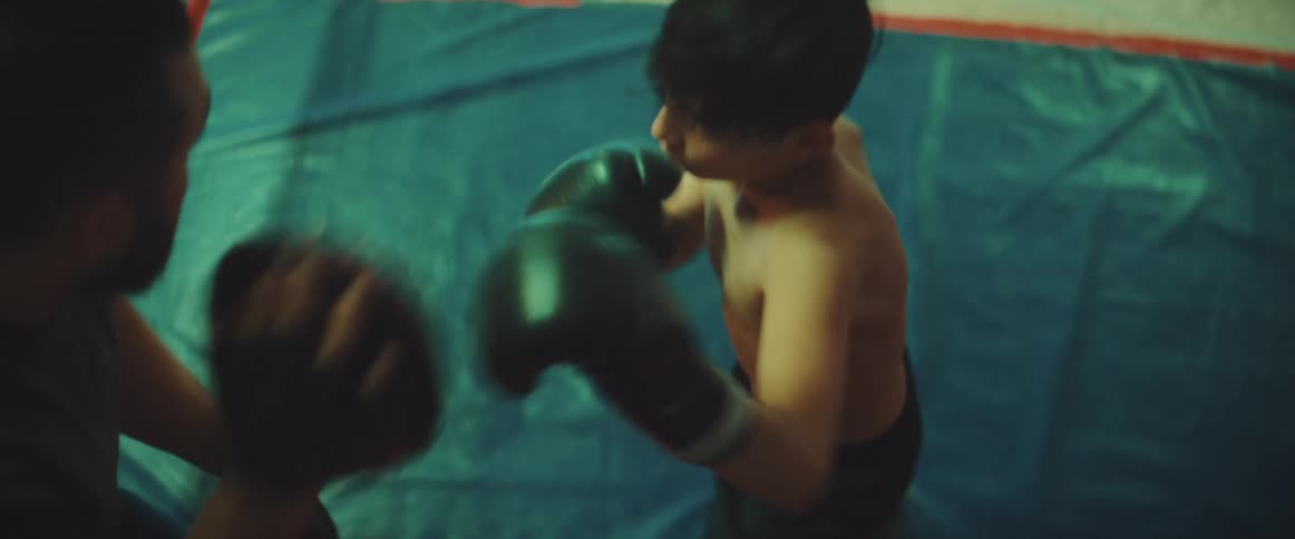 Boy sparring with an adult coach on a boxing ring at the gym