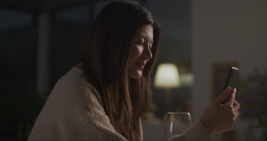 Woman smiles while conversing via smartphone video call at table