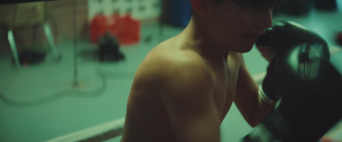 A boy practices boxing by striking the boxing mitts being positioned by a trainer