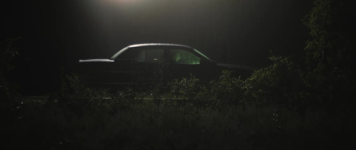 A woman sits in a parked car at night as rain pours down