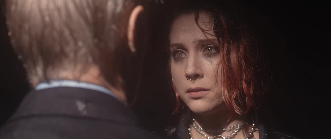 A sad looking teenager in the rain walks towards a man and throws her arms around him and hugs him