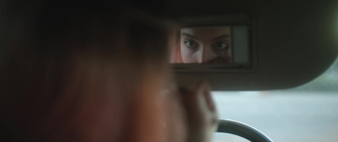 A young woman is inside of her car and putting on some makeup