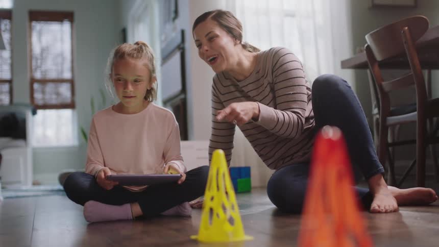 Mother and daughter play with a control remote toy on the floor of the living room