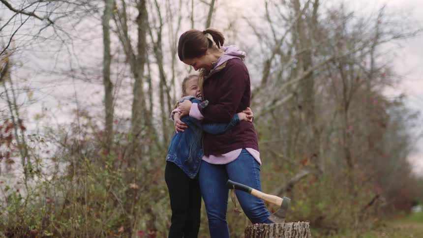 A daughter and mother hugging near a wooded area