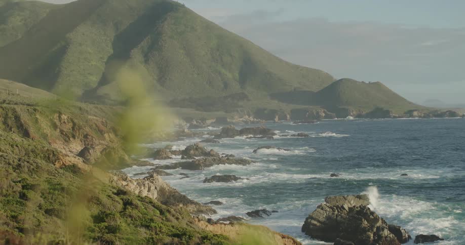 Waves roll toward craggy shore bordered by mountain