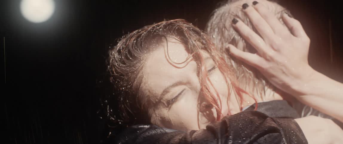 Redheaded crying woman steps forward to hug man as they stand in the rain at night