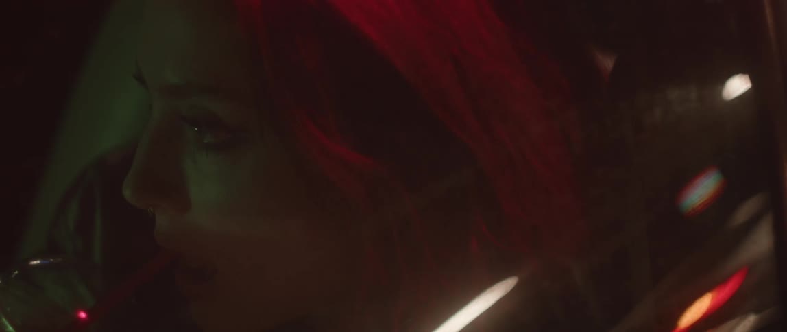 Close up of the face of a woman drinking soda while sitting on a parked car at night